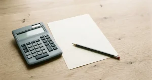 Taschenrechner auf einem Schreibtisch neben einem Blatt mit abstrakten Kästchen und einem Stift.